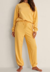 Felpa gialla con set di jogger coordinati realizzati in tessuto morbido e leggero. Presenta un collo rotondo, polsini elasticizzati e vita con cordino.