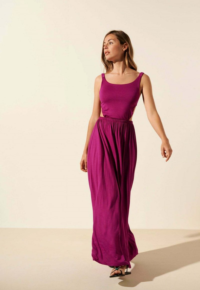 Robe maxi violette avec un haut ajusté et une taille élastique, fabriquée dans un matériau doux. Elle présente des bretelles fines et une jupe fluide.