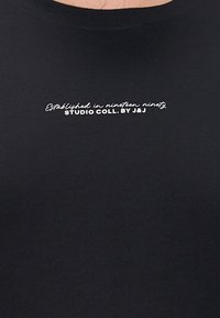 Crna majica kratkih rukava od mekog pamuka s okruglim izrezom, s bijelim natpisom "Osnovano tisuću devetsto devedeset Studija Coll. od J&J."