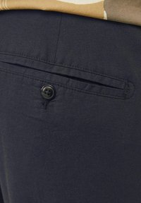 Pantalones de tela azul marino con un bolsillo trasero con un botón negro y detalles cosidos, mostrando una textura suave y ligera.