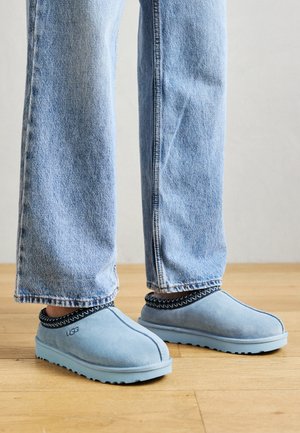 Heledad sinised sametist sussid, ümarate varvastega, mustade kunstniitidega kaela ümber ja tekstureeritud sinine tallaosa. Kantud heledate teksadega.