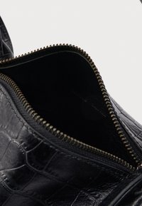 Borsa in pelle nera strutturata con cerniera metallica aperta che mostra l'interno vuoto su sfondo bianco.