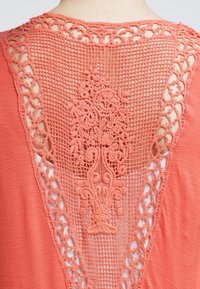 Coral top featuring a crochet lace back with floral pattern and diamond cutouts, soft texture, and a V-shaped neckline.
