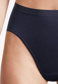 Un primo piano di una persona che indossa una lingerie alta senza cuciture di un blu navy scuro su pelle chiara, mostrando l'area dei fianchi e della parte inferiore della vita.
