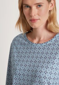 Top azzurro chiaro realizzato in tessuto morbido, con un motivo floreale in blu scuro e rosa, collo rotondo e vestibilità comoda.
