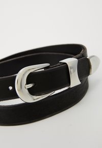 Cinturón de cuero negro enrollado con una hebilla de metal plateado, un lazo y una punta sobre un fondo blanco liso.