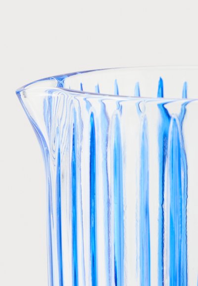 Pichet en verre transparent avec des rayures bleues verticales et un petit bec sur fond blanc.