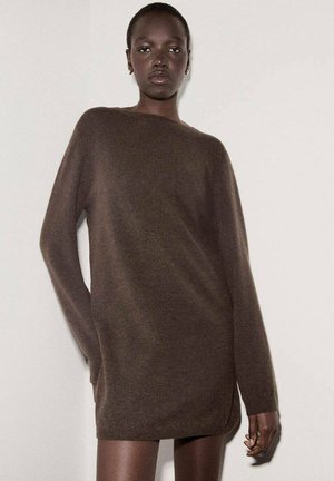 Un vestido suéter marrón de gran tamaño, hecho de material suave, con mangas largas, un cuello alto y aberturas laterales para mayor movilidad.