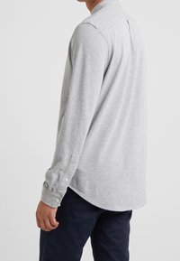 Harmaa pitkähiha paita, jossa on napillinen kalvosin, pehmeä pinta ja pyöristetty helma. Paidassa on myös takaosan yoke lisäämään muotoa.