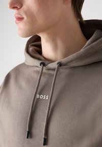 Sudadera con capucha en mezcla de algodón marrón. Cuenta con cordones ajustables con puntas negras y un logo "BOSS" blanco en el pecho.