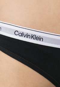 Zwarte katoenen bikini ondergoed met een witte elastische tailleband met het 'Calvin Klein' logo in het zwart erop gedrukt. Gladde textuur, lage taille ontwerp.