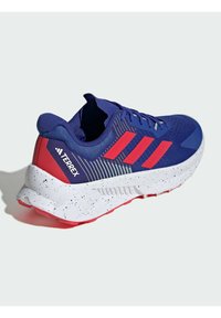 Blue athletic shoe with red accents, mesh upper, textured design, and white speckled outsole. Features three stripes logo on the side.