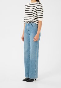 Pull rayé blanc et noir, jeans taille haute en denim bleu clair, ceinture noire avec une boucle en métal argenté, et escarpins noirs à bout pointu.