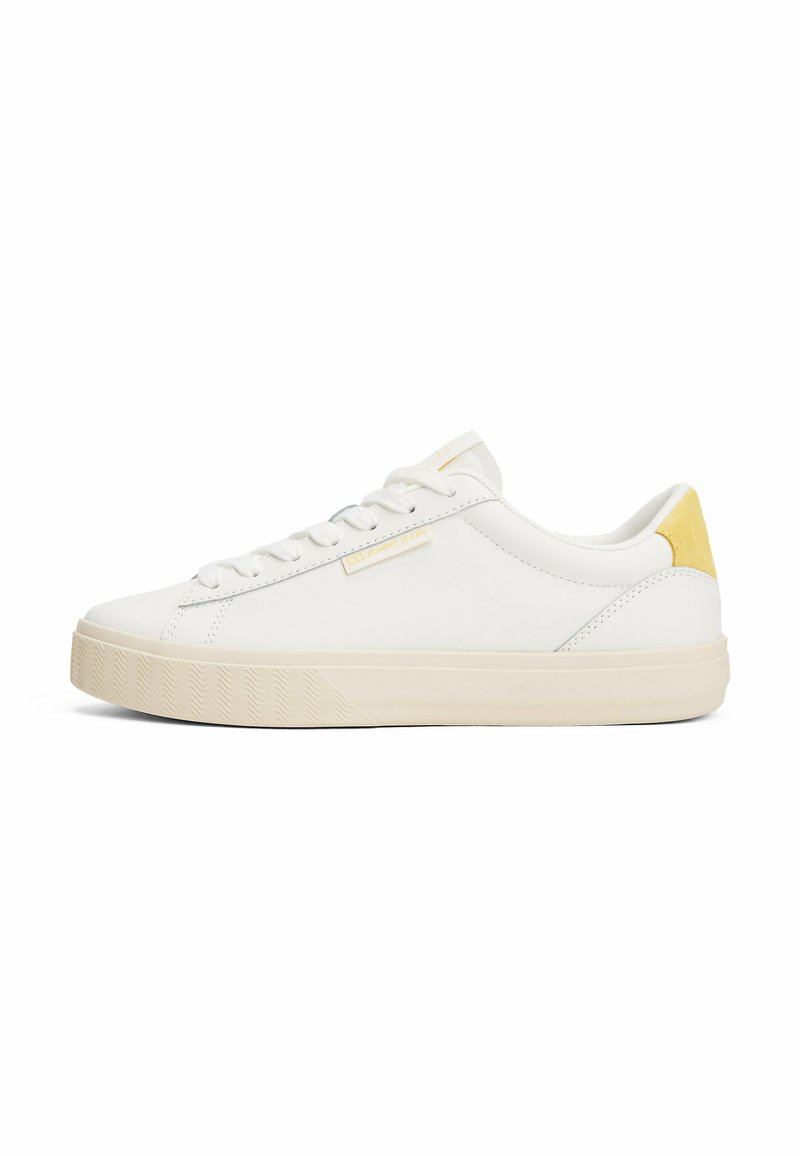 Sneaker en cuir blanc avec une semelle en caoutchouc texturé, des accents beiges et des lacets blancs plats. Présente un petit logo sur le côté.