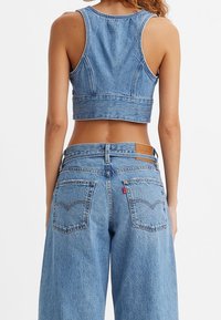 Ljusblå denimcroppad tanktop med breda band, i kombination med högmidjade, lösa jeans med bakfickor och sömnadsdetaljer.