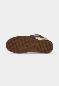 Semelle de chaussure avec motif de bande de roulement en caoutchouc marron présentant des formes circulaires et rectangulaires ainsi qu'un logo central, inclinée pour montrer le dessous et le côté.