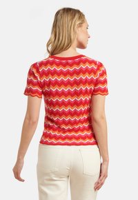 Rode trui met zigzagpatroon, korte mouwen en een ronde halslijn. Textuur details met ribbels, gecombineerd met lichte broek.