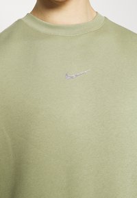 Närbild av en person som bär en ljusgrön crewneck-tröja med en liten vit Nike-logga på bröstet.