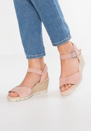 Jalat yang mengenakan sandal wedge merah jambu dengan tali pergelangan kaki dan gesper, dipadukan dengan celana jeans denim biru yang dilipat.