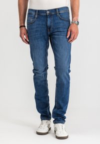 Niebieskie dżinsy o wąskim kroju, z pięcioma kieszeniami, subtelnymi przeszyciami i zapięciem na guziki. Połączone z białymi trampkami.