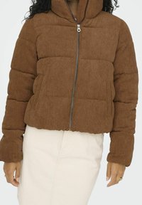 Bruine corduroy pufferjas met een hoge kraag, voorrits en elastische zoom; heeft een verticale ribbelstructuur en zijzakken.