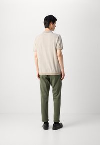 Beige rövid ujjú poloing texturált felülettel, olíva zöld nadrággal és fekete cipővel párosítva. Az öltözet hátulról van megjelenítve.