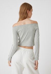 Graues, tailliertes Langarmoberteil mit schulterfreiem Design, das weiße Seitenstreifen aufweist. Der Stoff ist glatt und leicht.