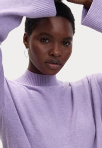 Lila Strickpullover mit hohem Rippenkragen und weiten Ärmeln, der über eine weiche Textur und minimale Details verfügt.