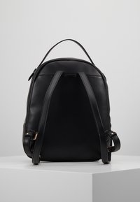 Mochila de cuero negra con forma redondeada, correas ajustables y un asa en la parte superior. Textura suave con un hardware mínimo y sin patrones visibles.