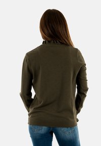 Maglione verde oliva con un motivo texturizzato, colletto a coste e maniche lunghe. Indossato con jeans di denim blu, che mostrano una silhouette aderente.