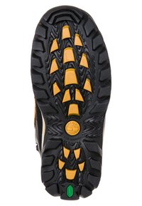 Černá gumová podrážka s žlutými trakčními hroty, s texturovaným vzorem a zeleným akcentem. Kulaté logo ražené poblíž paty.