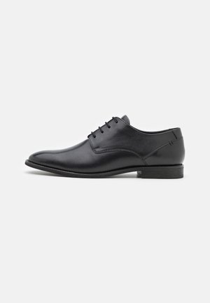 Black leather dress shoe with a smooth texture, pointed toe, low heel, and six eyelets for lace closure. Simple design without embellishments.