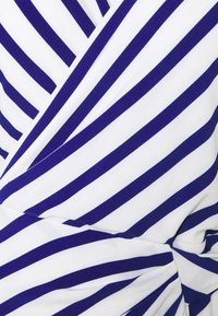 Tessuto a strisce con colori alternati blu navy scuro e bianco, caratterizzato da una trama morbida e un design avvolgente che crea effetti di drappeggio.