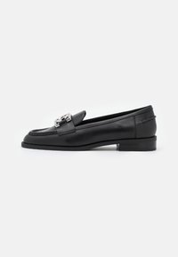 Mocassins en cuir noir avec des détails cousus et un accent en métal argenté. Talon bas rectangulaire avec une finition lisse et brillante.