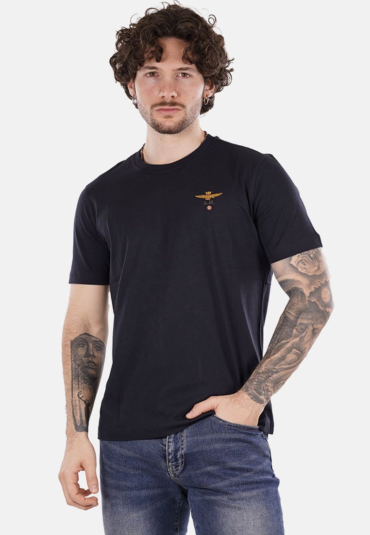 T-shirt in cotone blu navy con scollo rotondo e maniche corte, caratterizzato da un logo di aquila ricamato sul petto. Vestibilità strutturata.