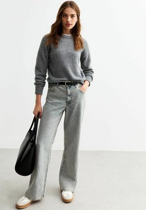 Pull en maille gris avec un col rond, associé à un jean large à taille haute en denim délavé clair. Ceinture noire et sac fourre-tout noir inclus.