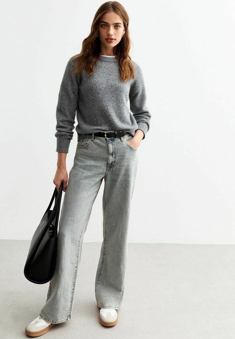 Maglione grigio a maglia con scollatura rotonda, abbinato a jeans a vita alta in denim chiaro e a gamba larga. Inclusi una cintura nera e una borsa tote nera.