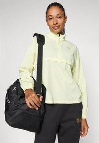 Gul, lätt tröja med hög krage och halvblixtlås, ihopparad med svart accessoarväska med nätpanel och Puma-logotyp.