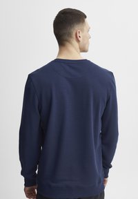 Tamsiai mėlynas megztinis su storu, tekstūruotu audiniu, su dryžuotu apykakle ir rankogaliais. Paprastas dizainas, be matomų logotipų ar raštų.