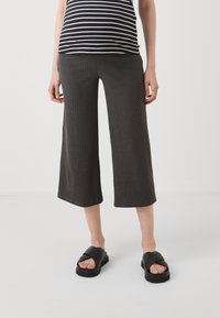 Sivé, rebrované culottes s širokým strihom, skombinované s čiernymi šľapkami. Pruhovaný top je viditeľný nad pásom. Jednoduchý, neformálny dizajn.