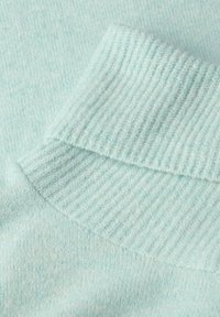Jasnoniebieska dzianina z prążkowanym kołnierzem; miękka tekstura, subtelny melanżowy wzór oraz złożony brzeg kołnierza.