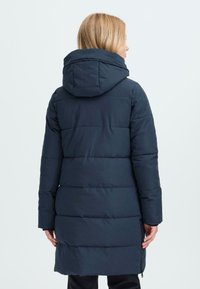Marineblå pufferjakke med hette, med vertikale quiltepaneler, lange ermer og sidelommer med glidelås. Glatt overflate og lett isolasjon.
