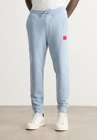 Svetlo modré tepláky vyrobené z mäkkej látky, s elastickým pásom na šnúrku, bočnými vreckami a červenou logom nášivkou.