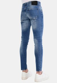 Slanke blauwe denim jeans met een vervaagde wassing, gestikte details, meerdere zakken en een zwart lederen label op de achterzijde van de tailleband.