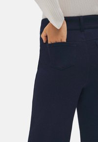 Pantalones azul marino de corte slim, con un bolsillo trasero y una textura suave. La cintura está asegurada y la tela es ligera y elástica.