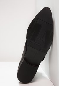 Suela de zapato negra con goma texturizada, que presenta una marca destacada y un borde superior liso. Talla 37 indicada en la plantilla.