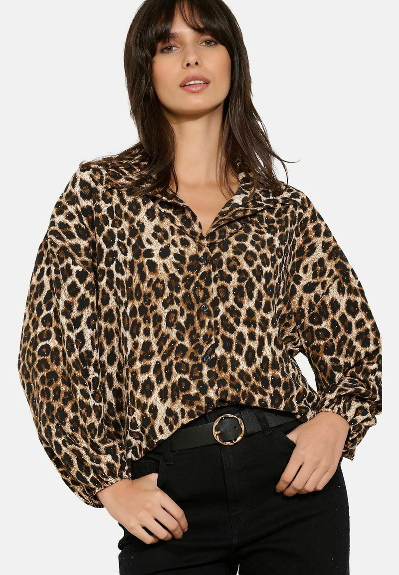 Mujer vistiendo una blusa de botones holgada con estampado de leopardo y mangas abullonadas, metida en pantalones negros con un cinturón de hebilla dorada redonda.