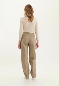 Pantalons beiges taille haute au design droit, avec deux poches arrière et un devant plissé, associés à un haut ajusté à manches longues.