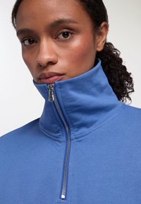Felpa blu con zip e colletto alto, realizzata in tessuto morbido. Presenta una zip argentata e una texture liscia.