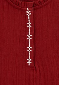 Top in tessuto rosso con scollatura arricciata, dotato di una patta ricamata bianca al centro. Materiale morbido e dalla texture piacevole.